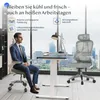 A man in a suit sits in an ergonomic office chair next to a standing desk with a computer and lamp. Another ergonomic chair is visible in the background. Produktbild-Vorschau