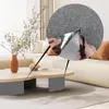 A living room scene with a sofa, coffee table, and a vase of flowers. A close-up inset shows hands cutting a gray textured mat with scissors. Produktbild-Vorschau