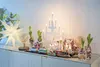 A Christmas-themed display on a white cabinet, featuring a star light, a vintage-style lamp, potted hyacinths in decorative holders, a toy train, and a tiered candle holder. Podgląd zdjęcia produktu