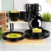 A collection of black dinnerware, including bowls, plates, and mugs, is displayed on a countertop and a shelf. Produktbild-Vorschau