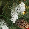 A close-up view of artificial Christmas tree branches with snow-like flocking, pinecones, and red berries, along with a green string of lights. Produktbild-Vorschau