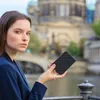 A woman holding a portable hard drive in front of a blurred cityscape. Produktbild-Vorschau