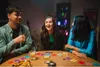 Three people are sitting around a table playing a card game. Produktbild-Vorschau