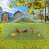 A large metal chicken coop with a mesh enclosure and a pitched roof, situated on a grassy lawn with two modern houses in the background. Several chickens and chicks are inside the coop. Produktbild-Vorschau
