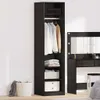 A tall, narrow black wardrobe with clothes hanging inside and folded items on shelves, next to a black vanity table with a mirror and lights. A white basket with a gray cloth is on the floor to the left. Produktbild-Vorschau