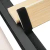 A close-up view of a bed frame component, showing a black metal frame with wooden slats and a black velcro strap attached. Podgląd zdjęcia produktu