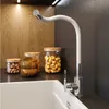 A modern kitchen sink area with a white flexible faucet, wooden bowls, and jars of food items. Produktbild-Vorschau