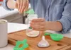 A person is preparing a baby bottle on a wooden cutting board. The scene includes a baby bottle, formula powder, a scoop, and a nipple. Náhľad obrázku produktu