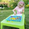 A young girl playing with colorful puzzle pieces on a table outdoors. Náhľad obrázku produktu