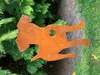A rusty metal garden stake shaped like a dog with a heart cut out of its body, placed in a garden setting with green foliage and grass. Produktbild-Vorschau