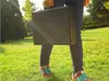 A person holding a portable charcoal grill in a grassy park. Produktbild-Vorschau