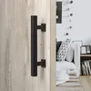 A black rectangular door handle is mounted on a light-colored wooden door, with a glimpse of a living room interior in the background. Produktbild-Vorschau