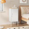 A white metal nightstand with a single door and a lock is placed next to a wooden bed frame. A floor lamp with an orange shade is to the left of the nightstand. Voir les images du produit