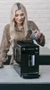 A woman is pouring coffee beans into a coffee machine. Produktbild-Vorschau