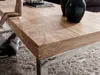 A close-up shot of a wooden coffee table with a metal frame, placed on a fluffy rug. A small wooden mannequin is sitting on the table. Produktbild-Vorschau