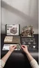 A ROKR 3D-Holz-Puzzle Murmelbahn / Kugelbahn 'Marble Spaceport' kit is laid out on a dark surface, with some parts assembled and others still on their frames. Hands are shown assembling a component. Podgląd zdjęcia produktu