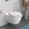 A modern white wall-mounted toilet with a marble-patterned seat, a toilet paper holder, and a vase with dried reeds in the background. Náhled obrázku produktu