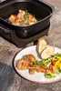 A meal of roasted chicken and salad is served on a wooden table next to an electric roaster. Anteprima dell’immagine prodotto