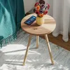 A small wooden side table with a vase of flowers and a smartphone on it, placed on a rug next to a teal blanket. Produktbild-Vorschau