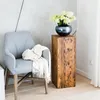 A chair with a blanket draped over it sits next to a wooden pedestal holding a vase of flowers. Anteprima dell’immagine prodotto