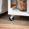 A close-up view of a white kitchen cart's caster wheel on a wooden floor. Náhled obrázku produktu