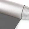 A close-up, rolled-up view of a dark gray blackout roller blind with a textured silver top edge. Produktbild-Vorschau