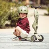 A young child wearing a helmet and a sweater crouches next to a scooter. Podgląd zdjęcia produktu