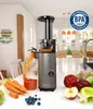 A slow juicer is shown in a kitchen setting, actively juicing carrots into a glass. Fruits and vegetables are arranged around the juicer. Produktbild-Vorschau