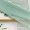 A close-up of a green sheer curtain draped over a book with a floral illustration. Produktbild-Vorschau