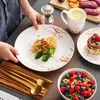 A table setting with a person serving a plate of pasta, a bowl of fruit, a mug, and a stack of pancakes. Náhled obrázku produktu