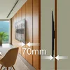 A TV wall mount is shown installed on a wooden paneled wall, with a TV attached. The image also includes a chair and a window with a view of mountains. Podgląd zdjęcia produktu