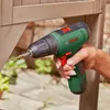 A hand is using a green Bosch cordless drill to screw into a wooden structure outdoors. Anteprima dell’immagine prodotto