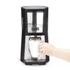 A coffee maker is brewing coffee into a white mug, with a hand holding the mug. Produktbild-Vorschau