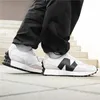 A person wearing black pants and white New Balance sneakers is walking on a paved surface with stairs in the background. Voir les images du produit