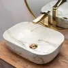 A close-up shot of a marble-patterned vessel sink with a gold faucet. Produktbild-Vorschau