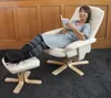 A woman is sitting in a recliner chair with her feet up on an ottoman, reading a book. Anteprima dell’immagine prodotto
