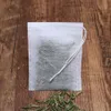 A white tea bag filled with green tea leaves sits on a wooden surface, with loose tea leaves scattered below. Produktbild-Vorschau