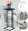 A black metal side table with a vase of pink roses on top, placed next to a grey armchair. Inset images show the table in different settings and a diagram with dimensions. Voir les images du produit