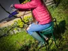 A person is gardening while sitting on a green stool. Produktbild-Vorschau