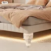 A close-up view of a bed with a white base and legs, covered in beige and gray bedding. Podgląd zdjęcia produktu