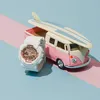 A white Baby-G watch is placed next to a pink and cream toy Volkswagen van with a surfboard on top, set against a blue and pink background. Anteprima dell’immagine prodotto