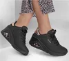 A pair of black Skechers sneakers with rose gold accents, worn by a person. Náhled obrázku produktu
