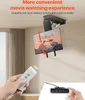 A hand holding a remote control is shown in the foreground, with a TV mounted on a motorized ceiling bracket in the midground. The TV is angled downwards, and text indicates its tilt range. A wired controller is visible in the bottom right corner. Podgląd zdjęcia produktu