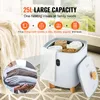 A white towel warmer bucket with a digital display, filled with rolled towels, placed on a patterned rug next to a bed with a cream-colored throw blanket. Náhled obrázku produktu