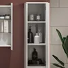 A close-up view of a white bathroom cabinet with several shelves, displaying various toiletries and decorative items. Produktbild-Vorschau