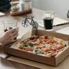 A pizza in a box on a table with drinks and a pizza cutter. Produktbild-Vorschau