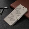 A gray butterfly-embossed phone case is shown on a textured black surface, next to a brown notebook and a pen. Produktbild-Vorschau