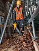 A construction worker is using a leaf blower to clear leaves from a wooden platform surrounded by scaffolding. Podgląd zdjęcia produktu