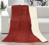 A red and beige blanket draped over a white sofa, with a plant and a black and white tree image in the background. Náhled obrázku produktu