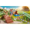 A PLAYMOBIL playset depicting a dog trainer with several dogs in an outdoor training area with agility equipment and dog houses. Produktbild-Vorschau